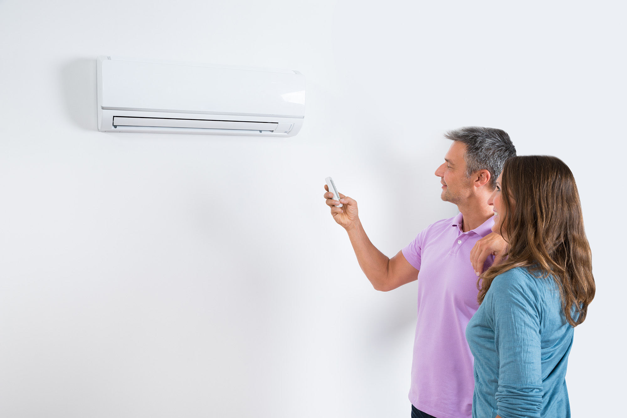 Mature Couple Standing In Front Of Air Conditioner And Adjusting The Temperature By Remote
